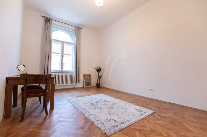 A room in a 3-room apartment with a wooden decor floor, a carpet, and a table.