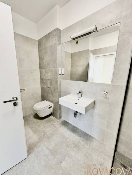 Bathroom with a sink and wall-mounted toilet, light tiles, large mirror.