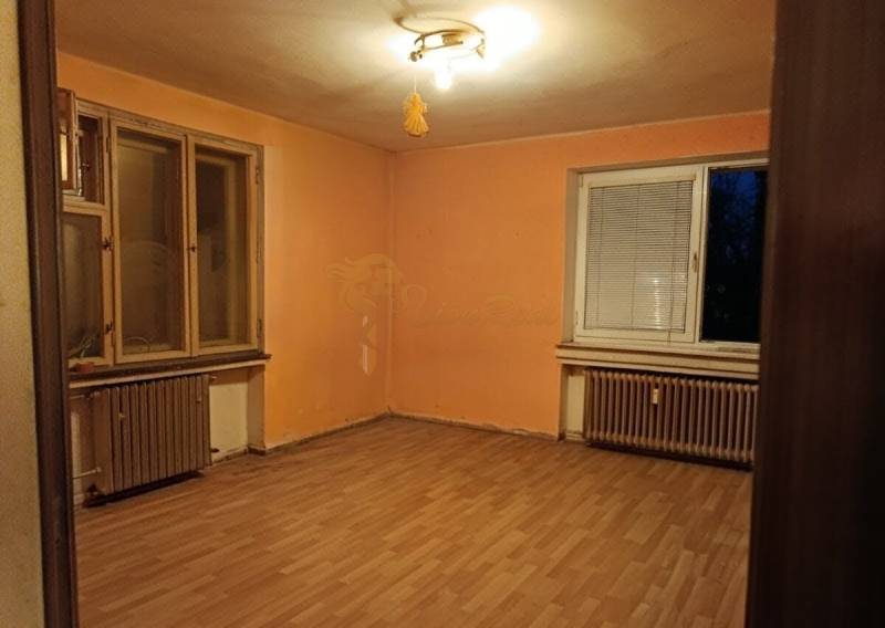 A room in a 2-room apartment, orange walls, wood-patterned floor, radiators.