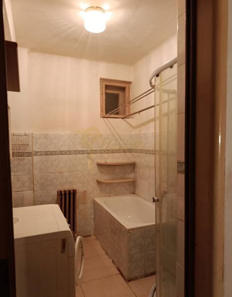 Bathroom with a bathtub and a washing machine in a 2-room apartment, tiles and a window.