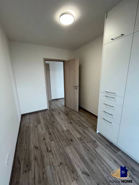 A room in a 3-room apartment with a wood-patterned floor and built-in storage space.