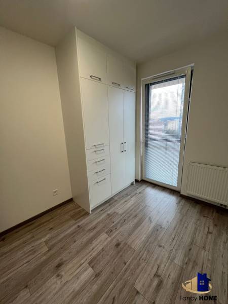 A room with a white wardrobe, a wooden-patterned floor, and balcony doors in a 3-room apartment.