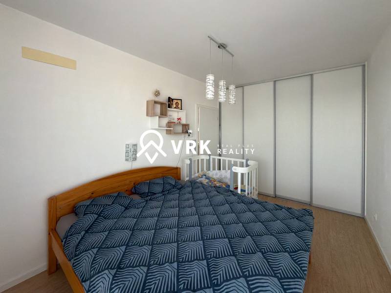 Bedroom in a 3-room apartment with a double bed, a baby crib, and a floor with a wooden decor.