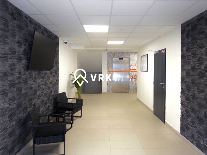 Hallway in a 3-room apartment with a TV on the wall and an elevator in the background.