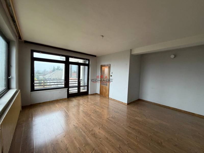 A room in a family house with a wooden-patterned floor and large windows overlooking the garden.