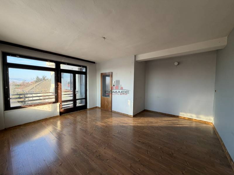 A room in a family house with a wooden decor floor, a large window, and a door.