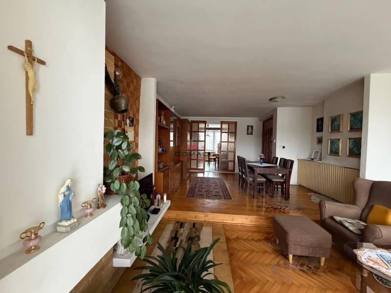 Living room in a family house with a wooden decor floor, a dining table, and a cross on the wall.
