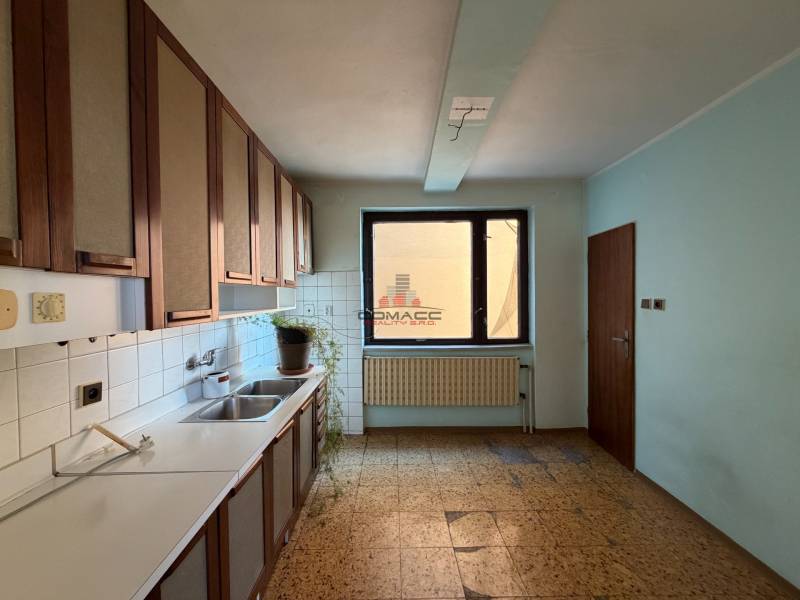 A kitchen in a family house with light blue walls and a window, and a floor with a wooden decor.