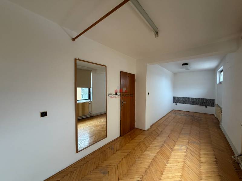 A room in a family house with a wooden decor floor, a mirror, and a window.