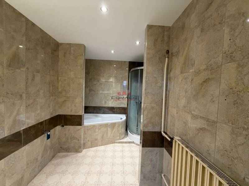 A bathroom in a family house with marble-look tiles and a corner bathtub.