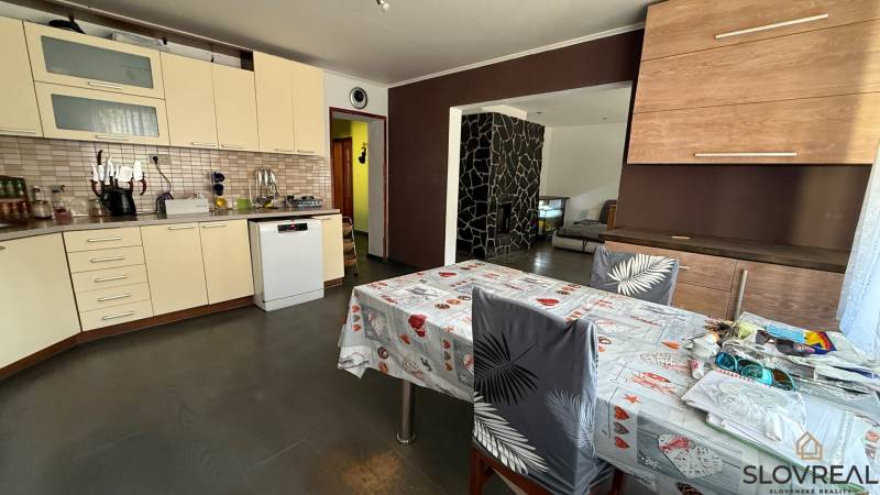 A kitchen in a family house with ceramic tiles, a dining table, and a dishwasher.