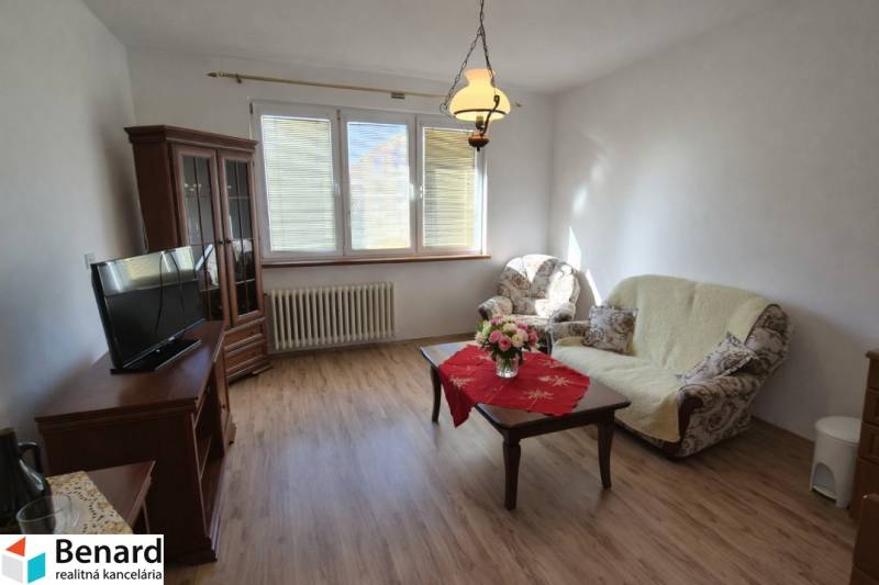 Living room in a two-room apartment with a wooden decor floor, comfortable furniture, and a decorative table.