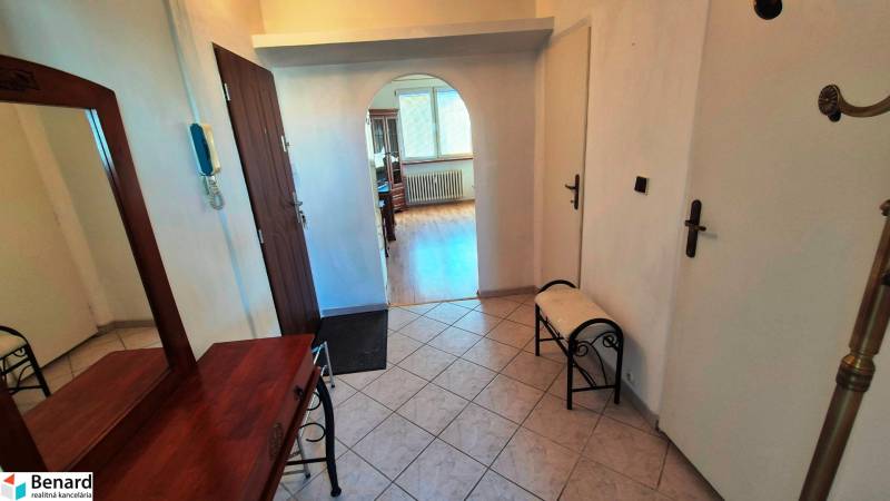 A hallway with an arched passage in a 2-room apartment, a floor with a wooden decor, a mirror, a bench.