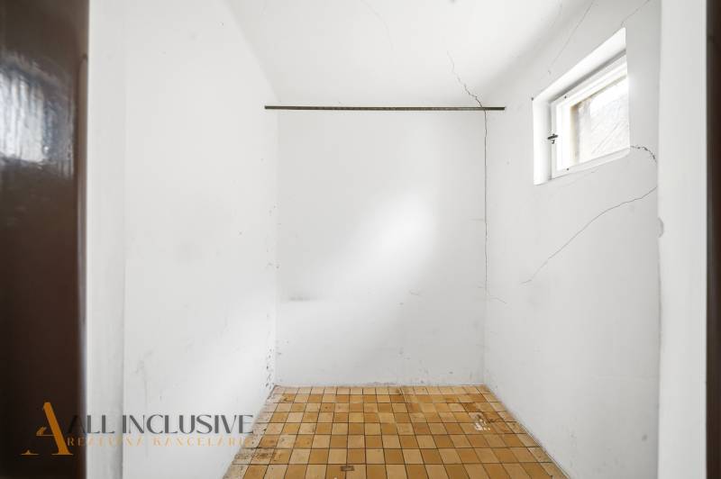 Empty room with a window, white walls, and tiled floor with cracks in a family house.