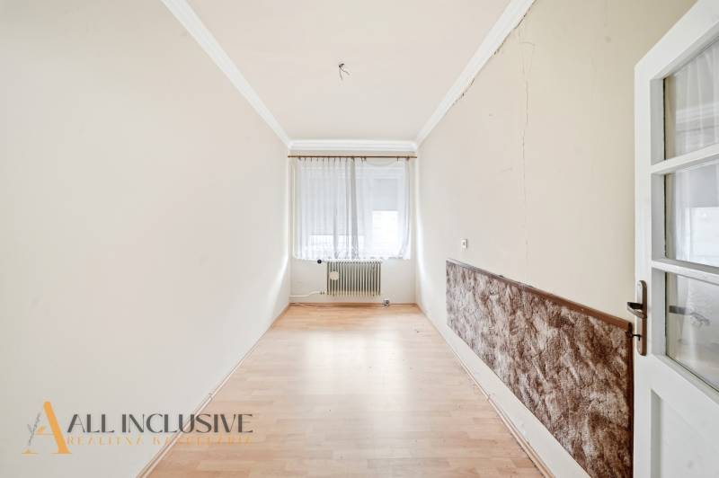 A narrow room with a wood-patterned floor, a window with curtains, a radiator.