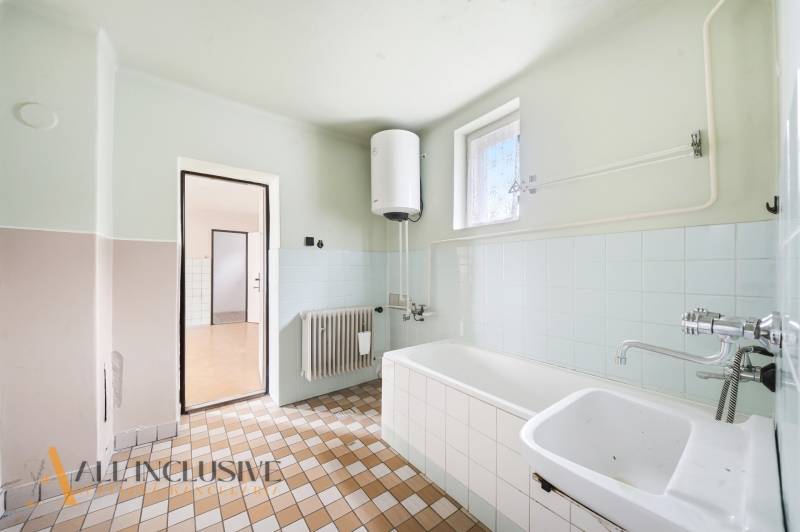 A bathroom in a family house with a shower, sink, radiator, and heating boiler.