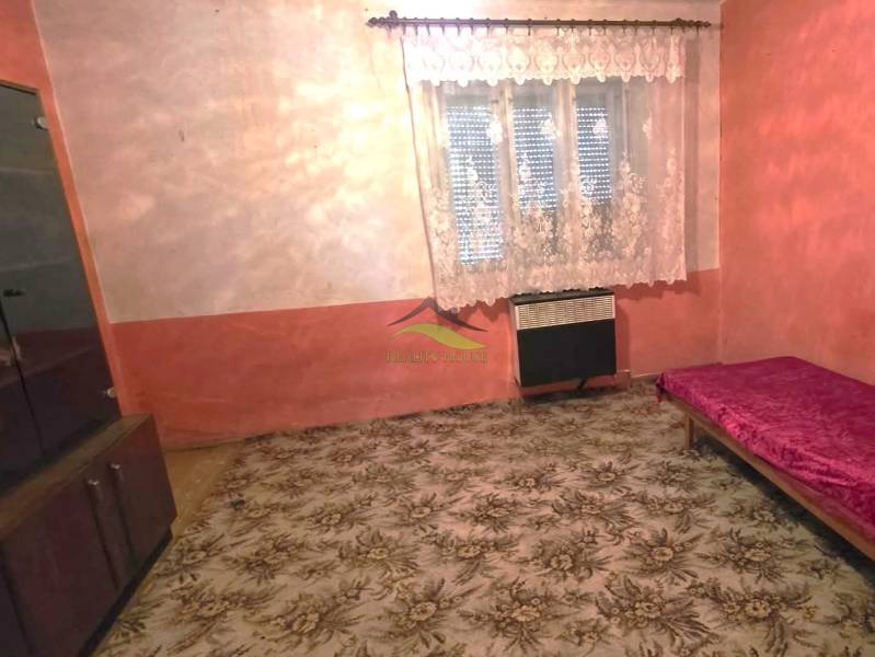 A room in a family house with a carpet, a bed, and a cabinet, with a curtain on the window.