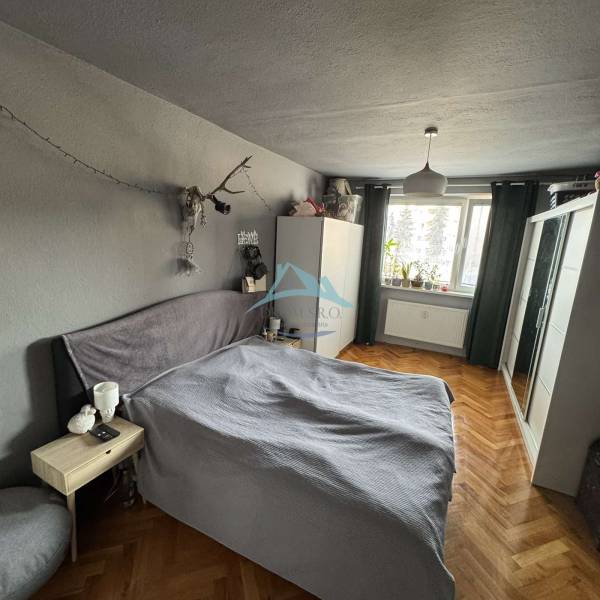 Bedroom in a 3-room apartment with a bed, wardrobe, and wooden decor flooring.