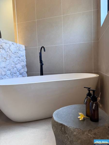 A bathroom in a family house with a bathtub, a stone-clad wall, and decorative bottles.