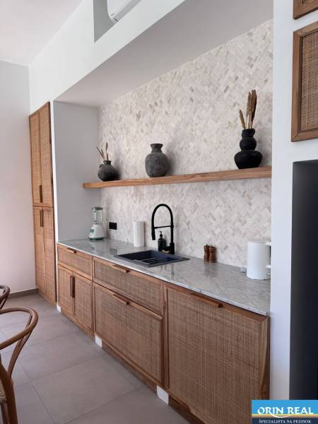A kitchen with a natural/organic design, a sink, an open shelf with ceramic decorative items.
