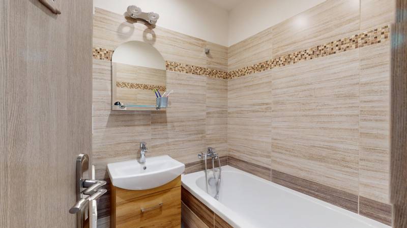 Bathroom in a two-room apartment with light tiles and a bathtub, cabinets under the sink.