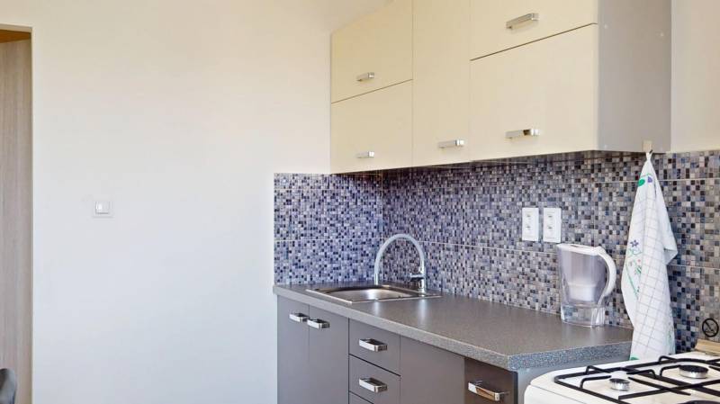 A kitchen with mosaic tiles in a 2-room apartment, with wooden decor kitchen cabinets.