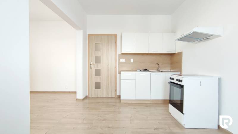 A kitchen in a 2-room apartment with white cabinets, a stove, and a wooden decor floor.