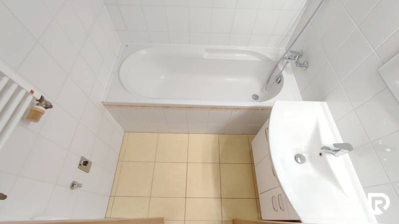Bathroom in a 2-room apartment with a bathtub, sink, and white tiles.