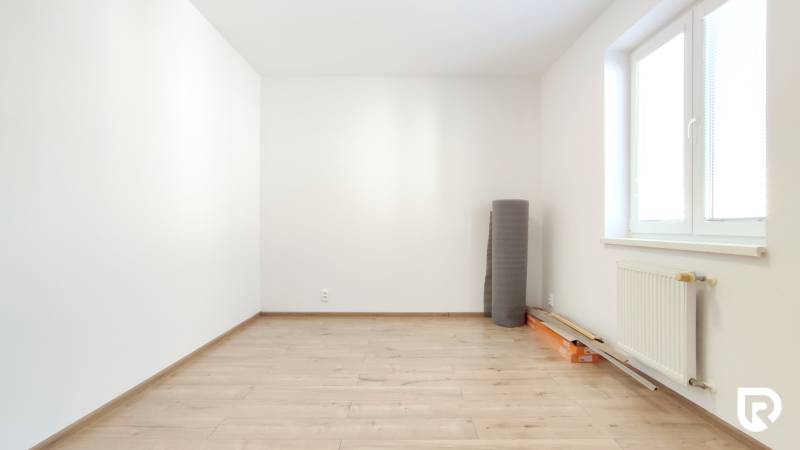 Empty room in a 2-room apartment with a wood-patterned floor and a radiator by the window.
