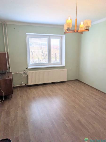 A room in a family house with a wood-patterned floor and a window with a radiator.