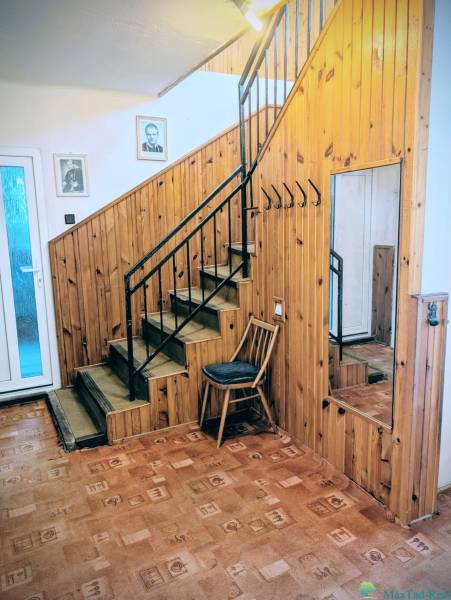 Interior of a family house with wooden paneling, a mirror, a staircase, and a floor with a wooden decor.