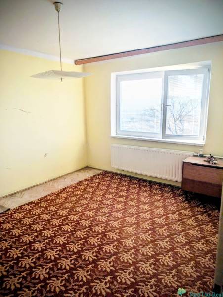 A room in a family house with a carpet, yellow walls, a table, and a ceiling light.