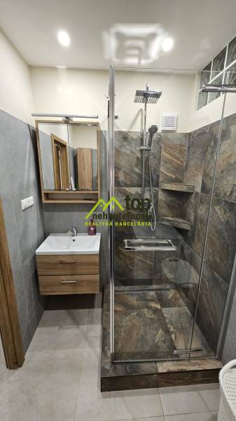 Bathroom in a 2-room apartment with a shower and a sink with a wooden decor.