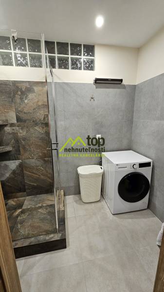 Bathroom with a shower and a washing machine in a 2-room apartment with tiled flooring.