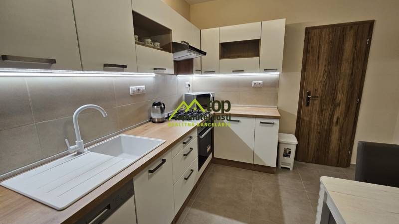 A kitchen in a 2-room apartment with white cabinets and a wooden decor floor.