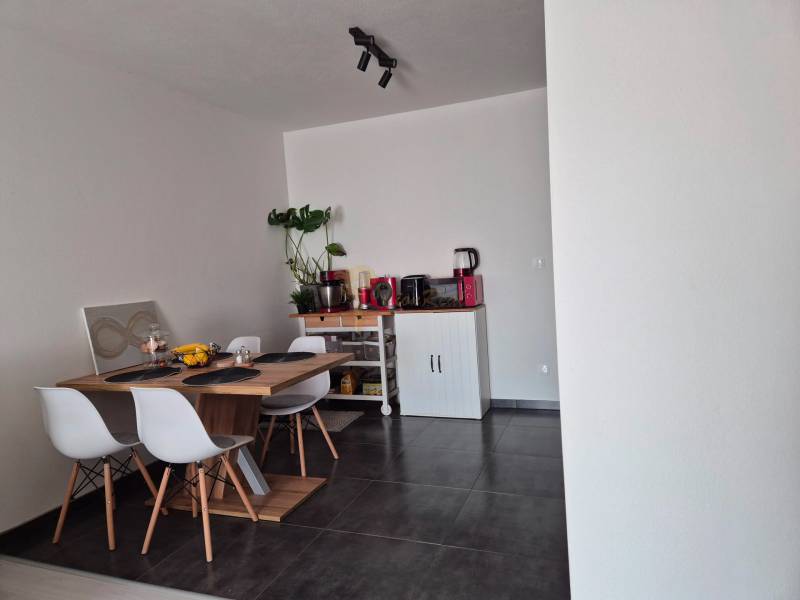 Dining area with a wooden table, four chairs, and a plant in a three-room apartment.