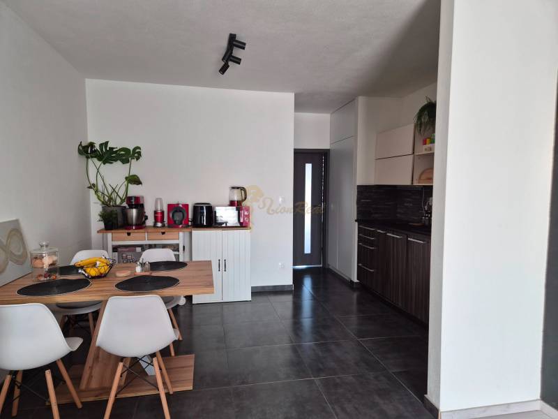 A kitchen in a 3-room apartment with a dining table, dark floor, and white chairs.