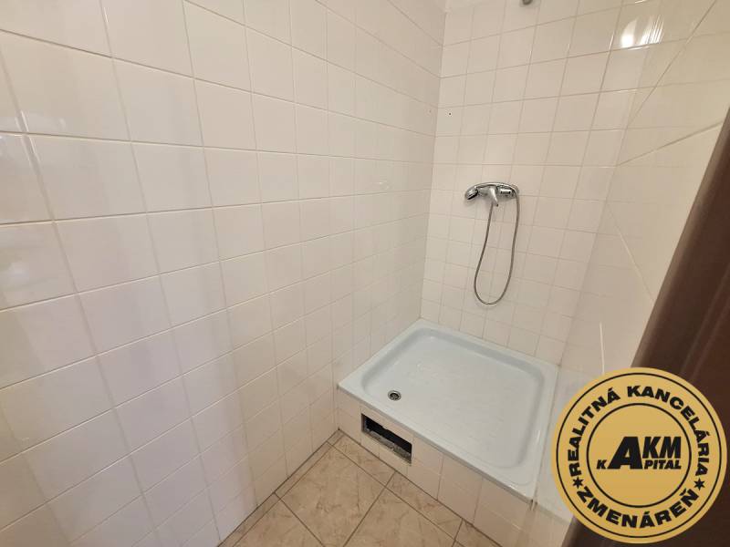 A shower corner with white tiles and flooring in an office.