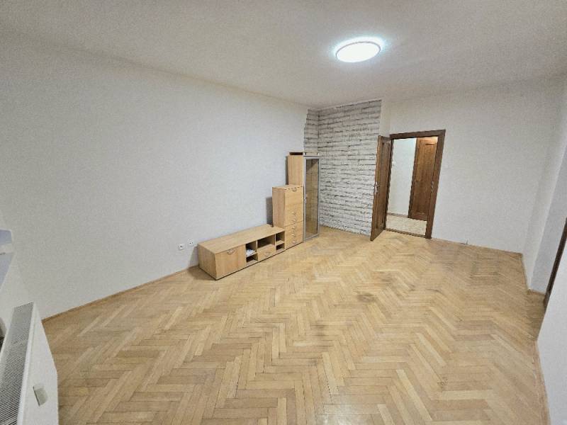 A bright room in a two-room apartment with a wood-decorated floor and furniture.