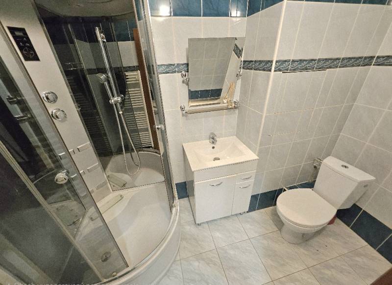 Bathroom in a 2-room apartment with a corner shower, sink, and toilet.