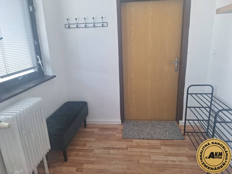 In a building with a wood-patterned floor, there is a bench, a radiator, and a wall-mounted coat rack.