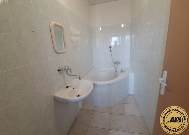 Bathroom in a building with a corner bathtub, white sink, and light tiles.