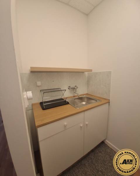 Kitchen corner with sink and drainer, building, light tiles, white cabinet.