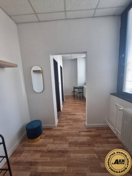 Interior of a building with wood-patterned flooring, chairs, mirror, white ceiling.
