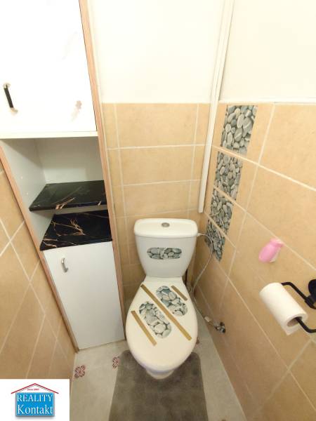 Toilet in a one-room apartment with stone decor on the tiles and toilet.