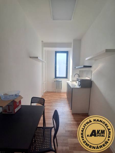 A narrow office with a black desk, chairs, and a wooden decor floor.