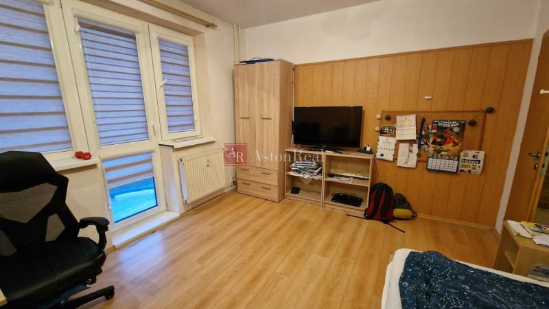 A room in a 3-room apartment with a wood-decor floor, a television, and an armchair.