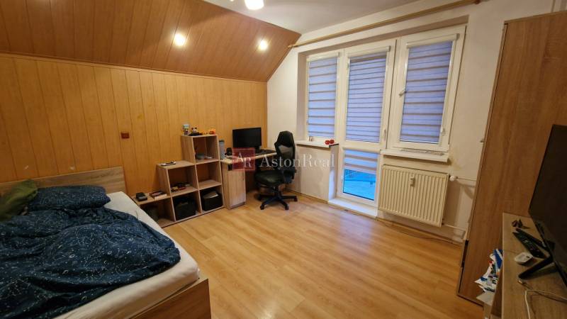 A bedroom in a three-room apartment with a wooden decor floor, a desk, and a bed.