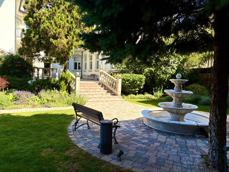 A garden with a fountain, bench, and greenery in front of the building.