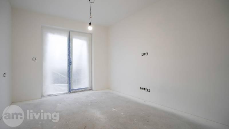An empty room in a family house with a hanging light bulb and closed doors to the terrace.